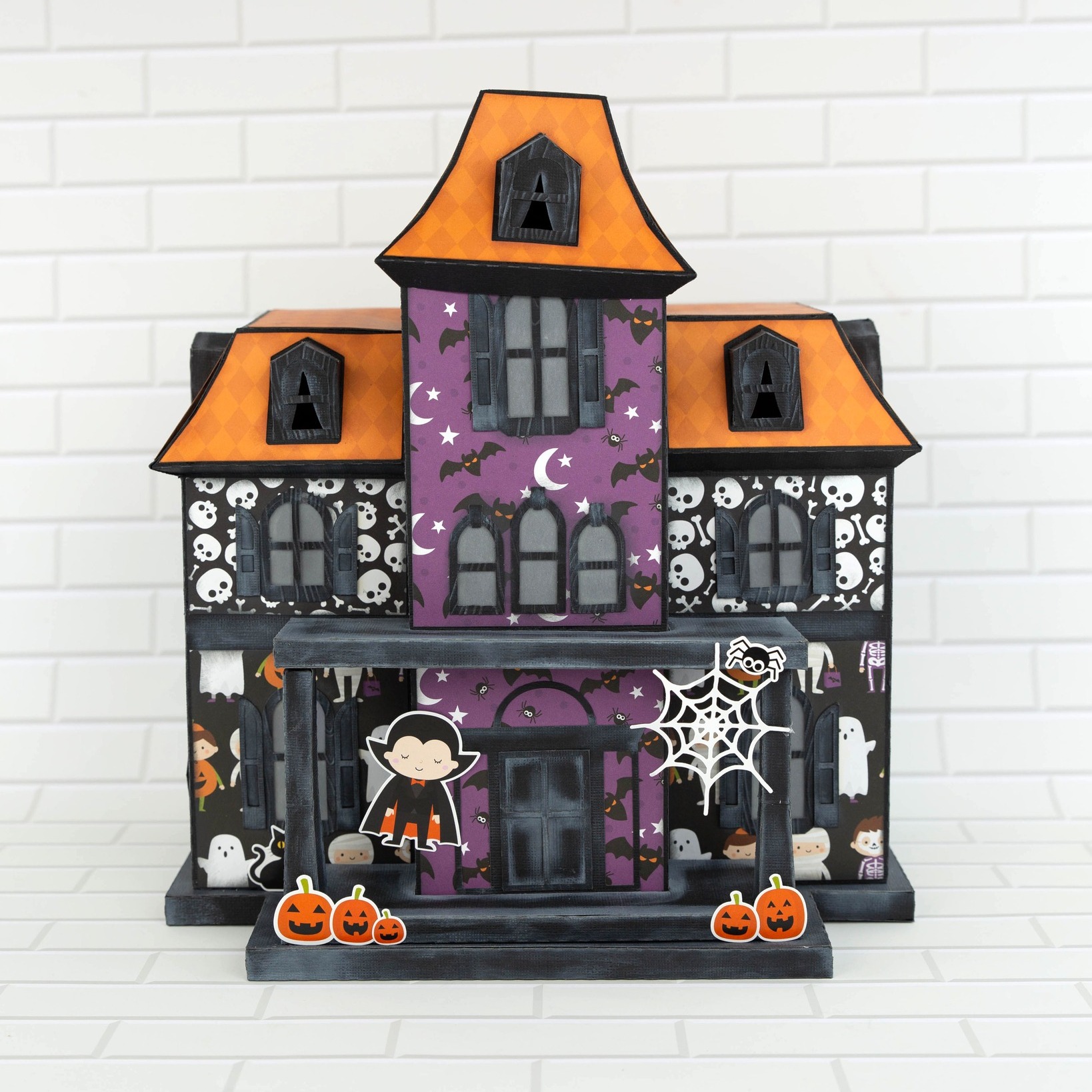 Paper crafted haunted house created with Echo Park Paper Co. Halloween Magic Collection and SVGcuts template, featuring orange roofs, purple and black patterned papers, and cute Halloween embellishments.