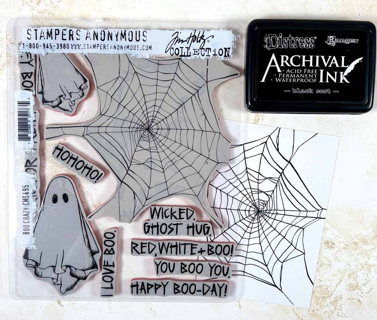 Step 1 of Spooky Treat Tags project by Heather Fischer showing Stampers Anonymous Boo Crazy CMS495 stamp set and Ranger Archival Ink Black Soot used to stamp cobweb images on white cardstock.